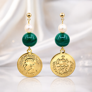 Pair of earrings with gold coins, green beads, and pearls on a reflective surface.