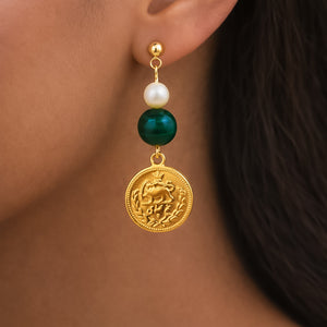 Close-up of an earring with a gold coin, pearl, and green stone on a person's ear.