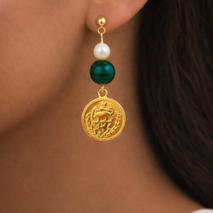 Close-up of an earring with a gold coin, pearl, and green stone on a person's ear.