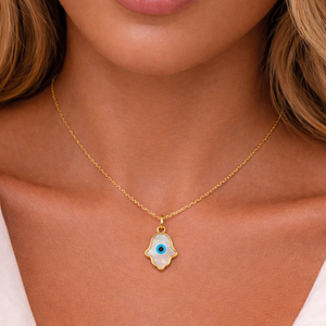 Gold necklace with a hamsa hand pendant featuring an eye design on a person wearing a white top.