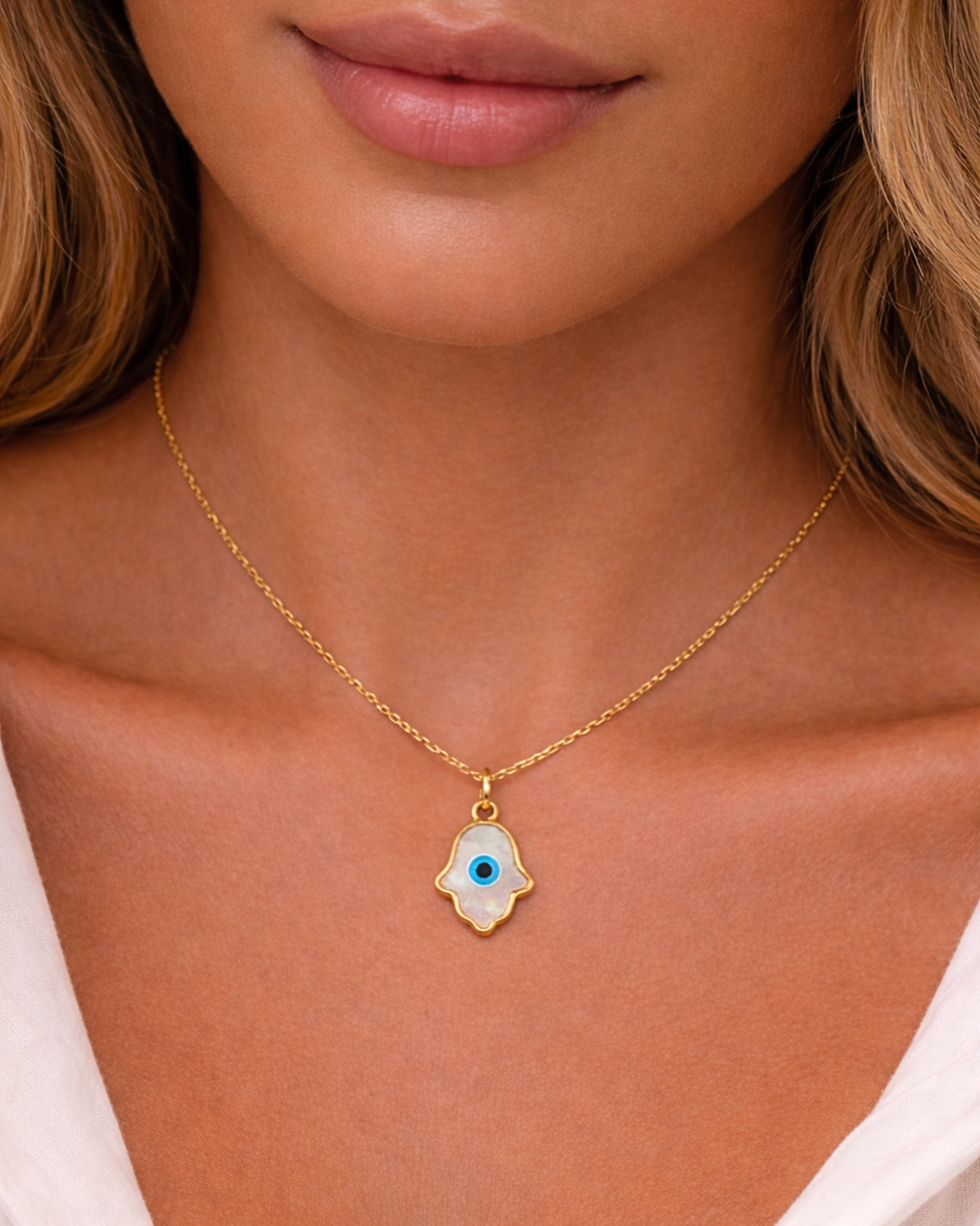 Gold necklace with a hamsa hand pendant featuring an eye design on a person wearing a white top.