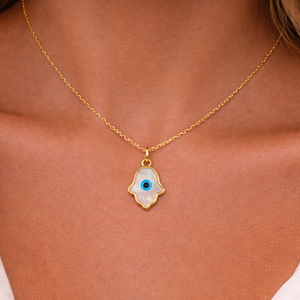 Gold necklace with a hamsa hand pendant featuring an eye design on a person wearing a white top.