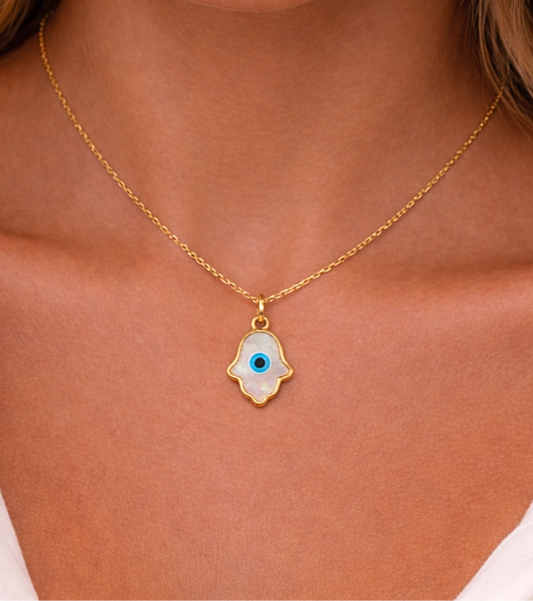 Gold necklace with a hamsa hand pendant featuring an eye design on a person wearing a white top.
