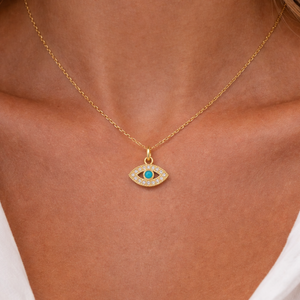 Gold necklace with an eye-shaped pendant on a person wearing a white top.