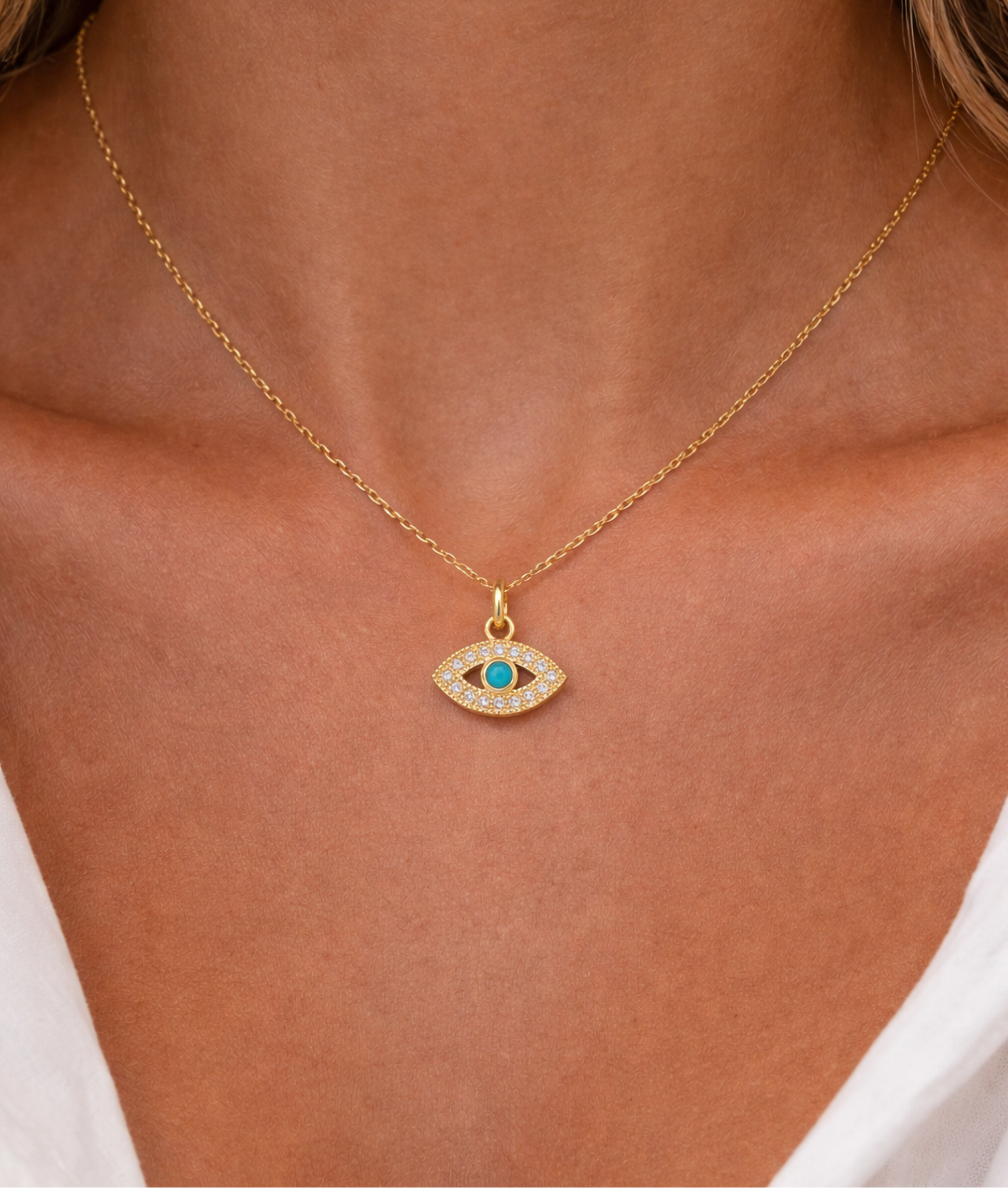 Gold necklace with an eye-shaped pendant on a person wearing a white top.