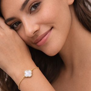 Woman wearing a gold bracelet with a clear stone on a neutral background