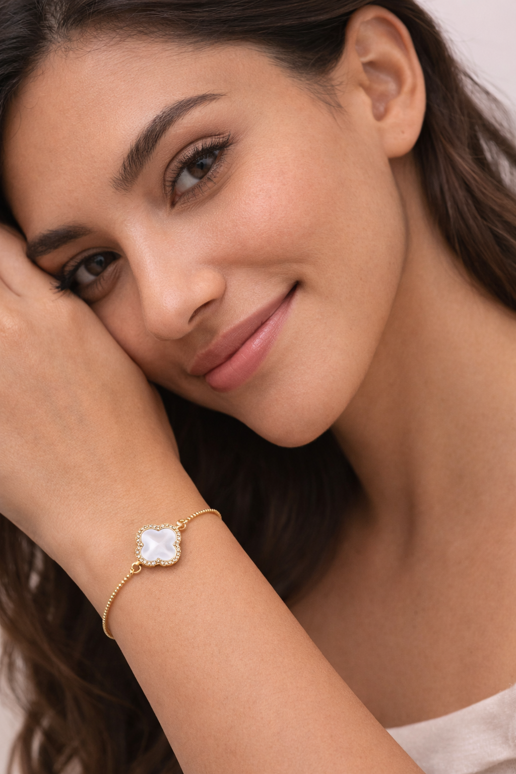 Woman wearing a gold bracelet with a clear stone on a neutral background