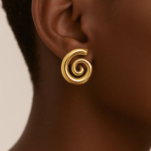 Gold spiral earring on a person's ear with a neutral background