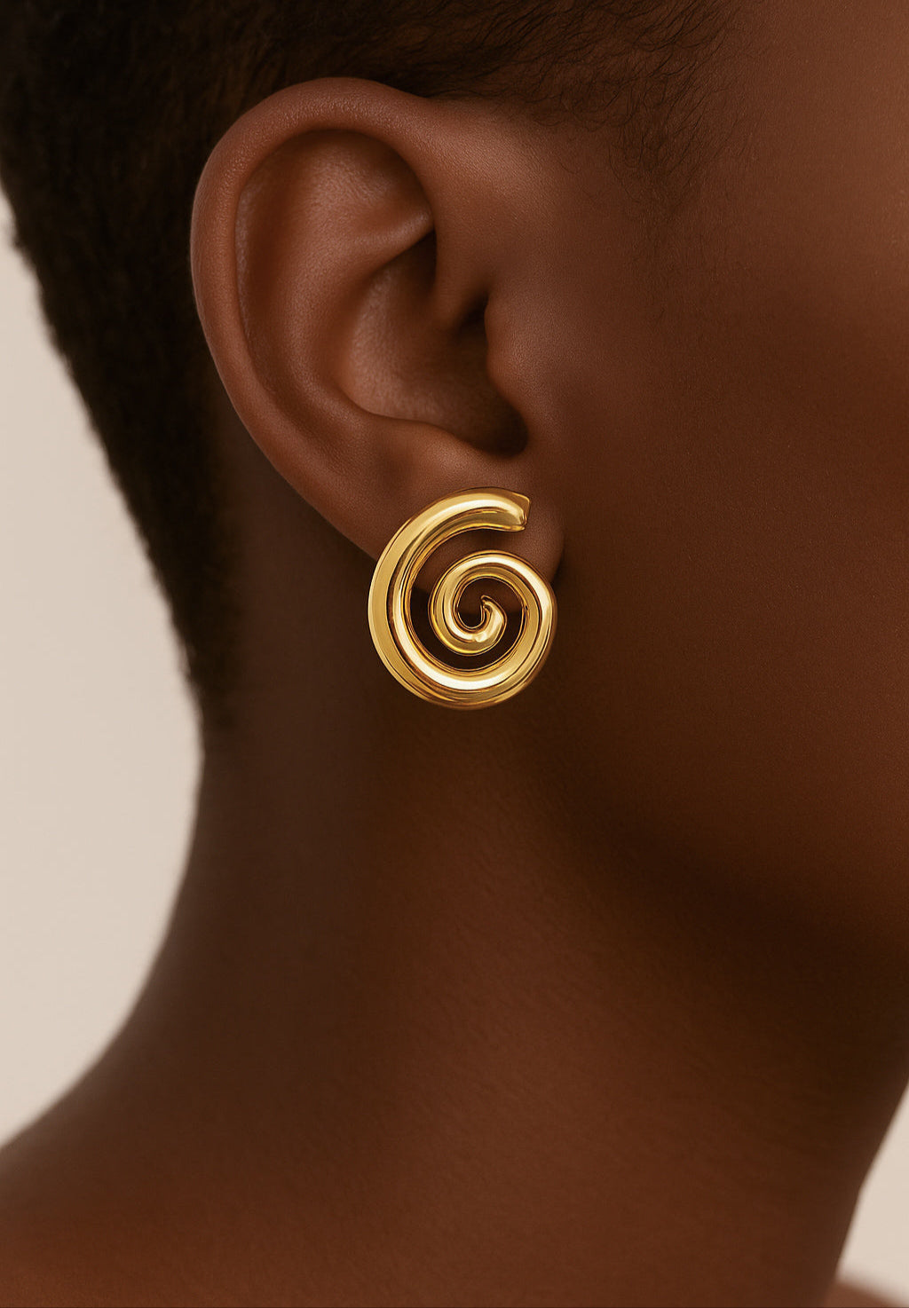 Gold spiral earring on a person's ear with a neutral background