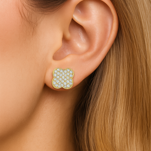 Close-up of an ear wearing a floral earring with gold and green stones.