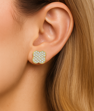 Close-up of an ear wearing a floral earring with gold and green stones.