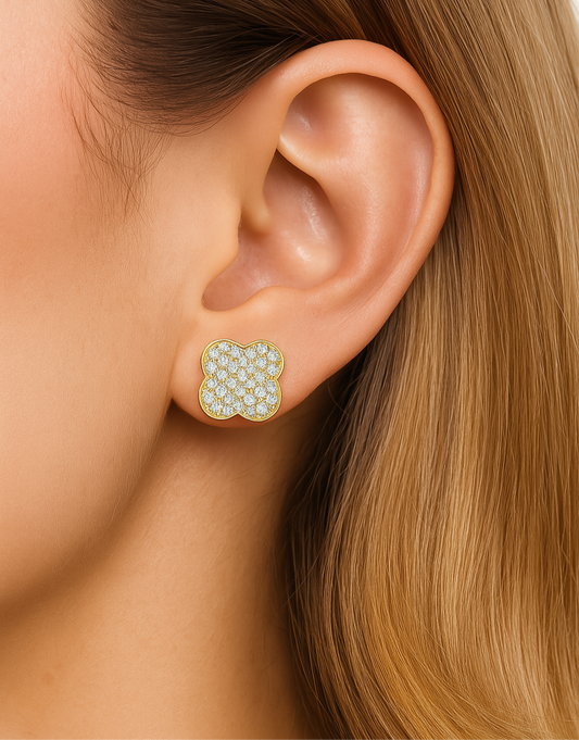 Close-up of an ear wearing a floral earring with gold and green stones.
