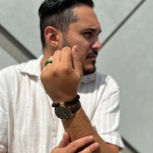 Man wearing a white shirt and multiple bracelets on his wrist, standing against a light-colored wall.