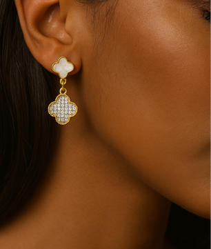 Close-up of a person wearing a gold and white clover-shaped earring.