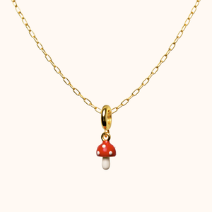 Gold necklace with a red and white mushroom pendant on a white background