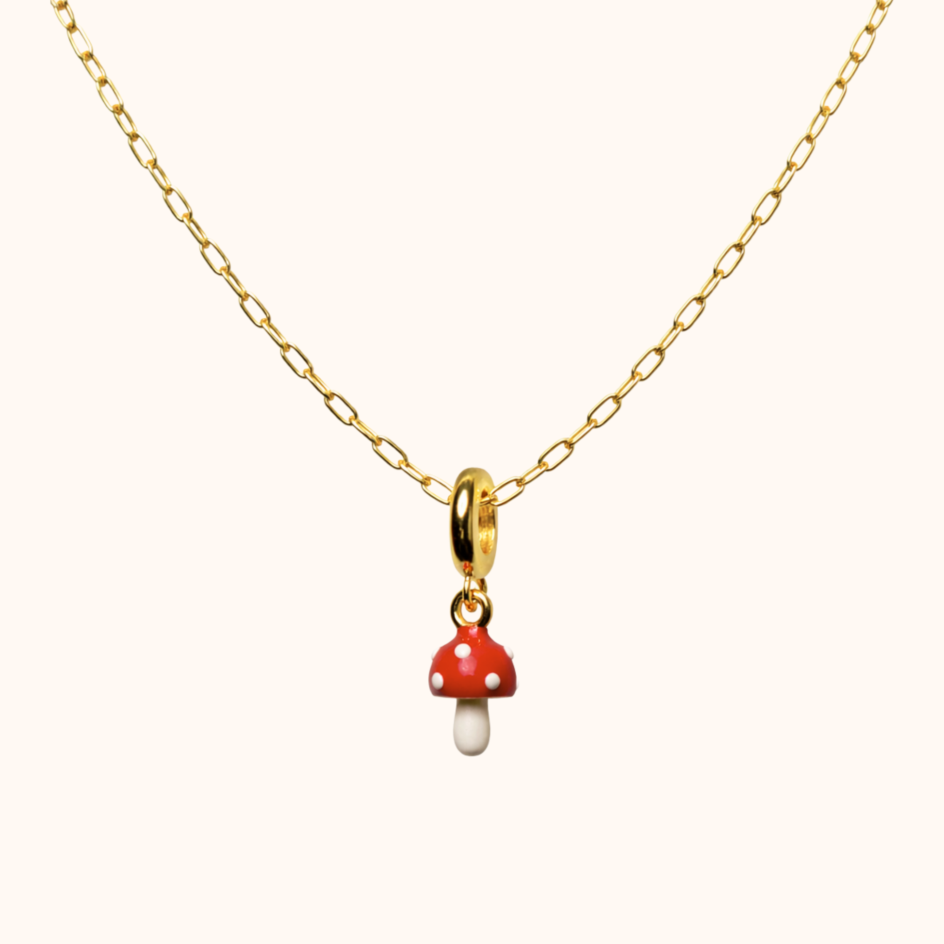 Gold necklace with a red and white mushroom pendant on a white background
