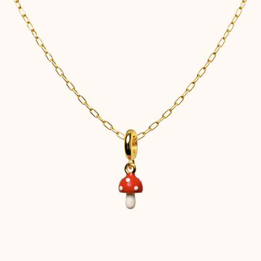 Gold necklace with a red and white mushroom pendant on a white background
