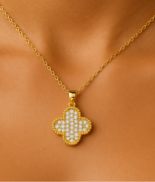 Gold necklace with a clover-shaped pendant on an orange fabric background