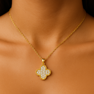 Gold necklace with a clover-shaped pendant on a person's neck against a neutral background