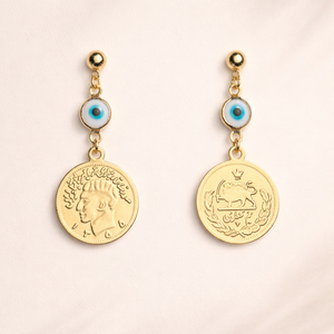 Pair of gold earrings with iranian coin designs on a light pink background