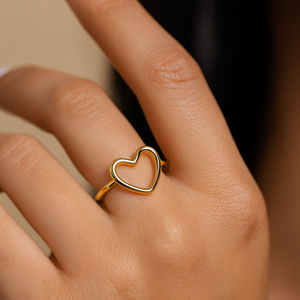 Gold heart-shaped ring on a person's finger with a neutral background