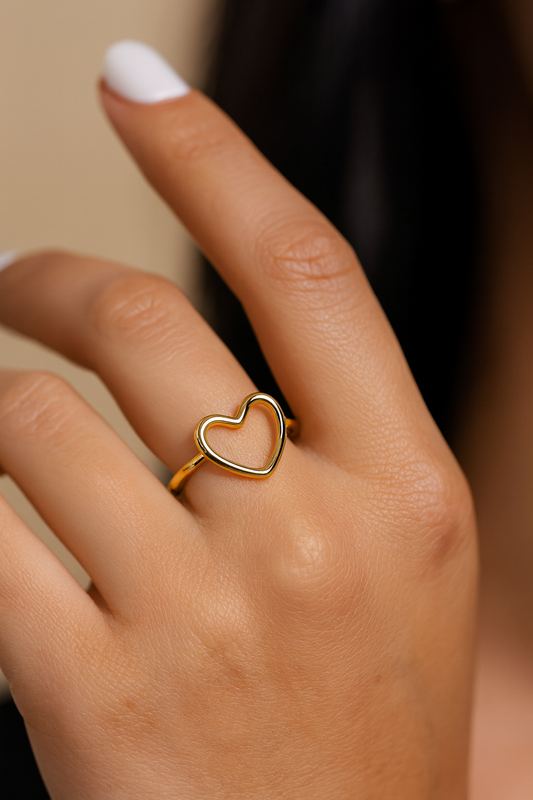 Gold heart-shaped ring on a person's finger with a neutral background