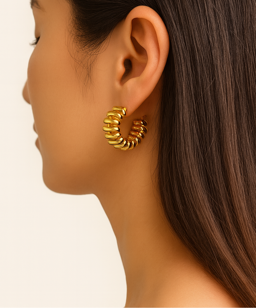 Gold hoop earring worn by a model on a plain background