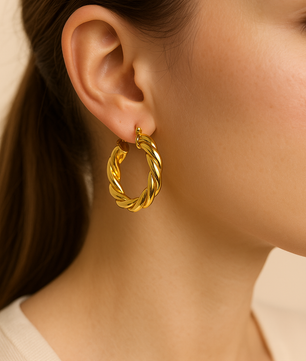 Close-up of a person wearing a gold hoop earring with a neutral background