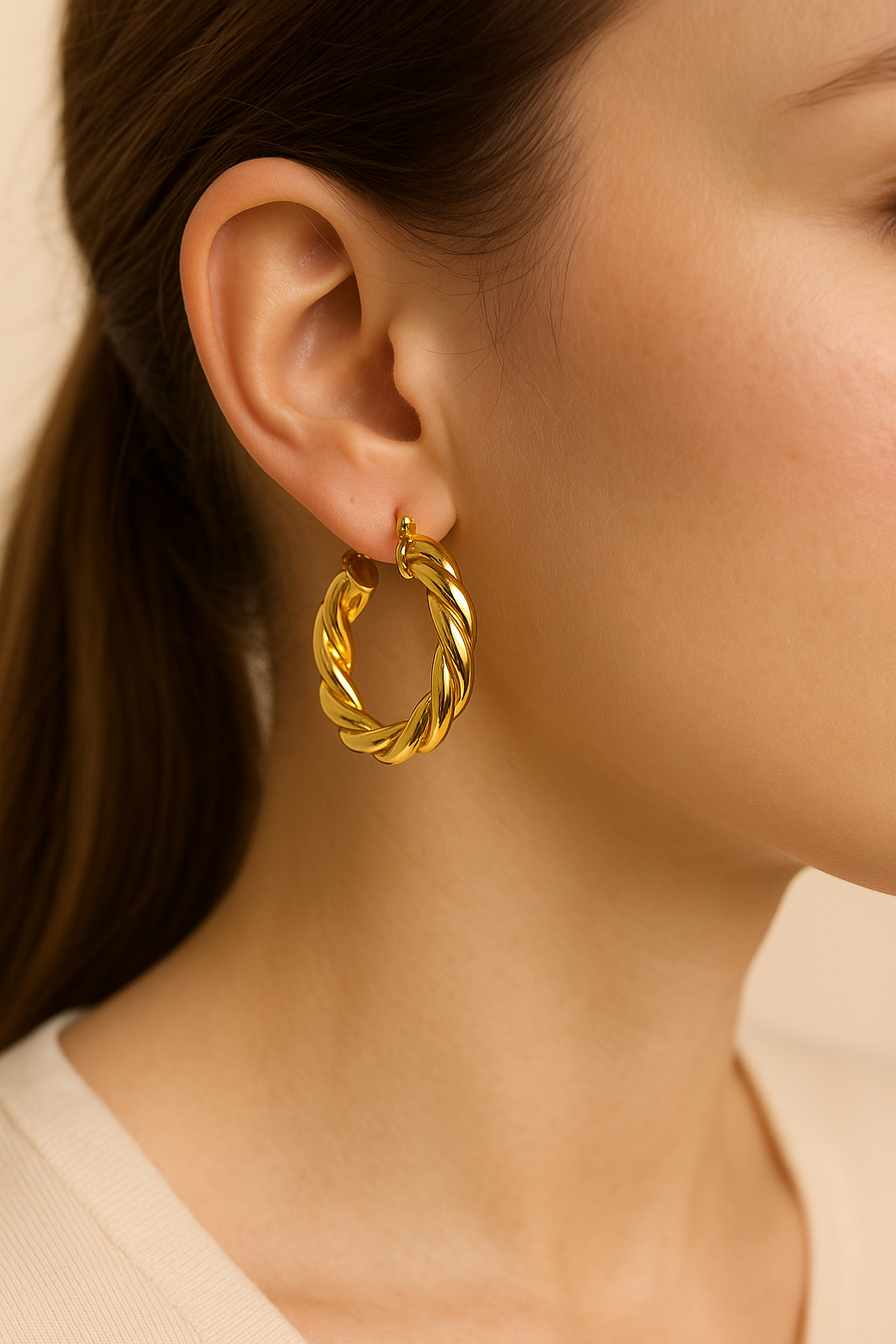 Close-up of a person wearing a gold hoop earring with a neutral background