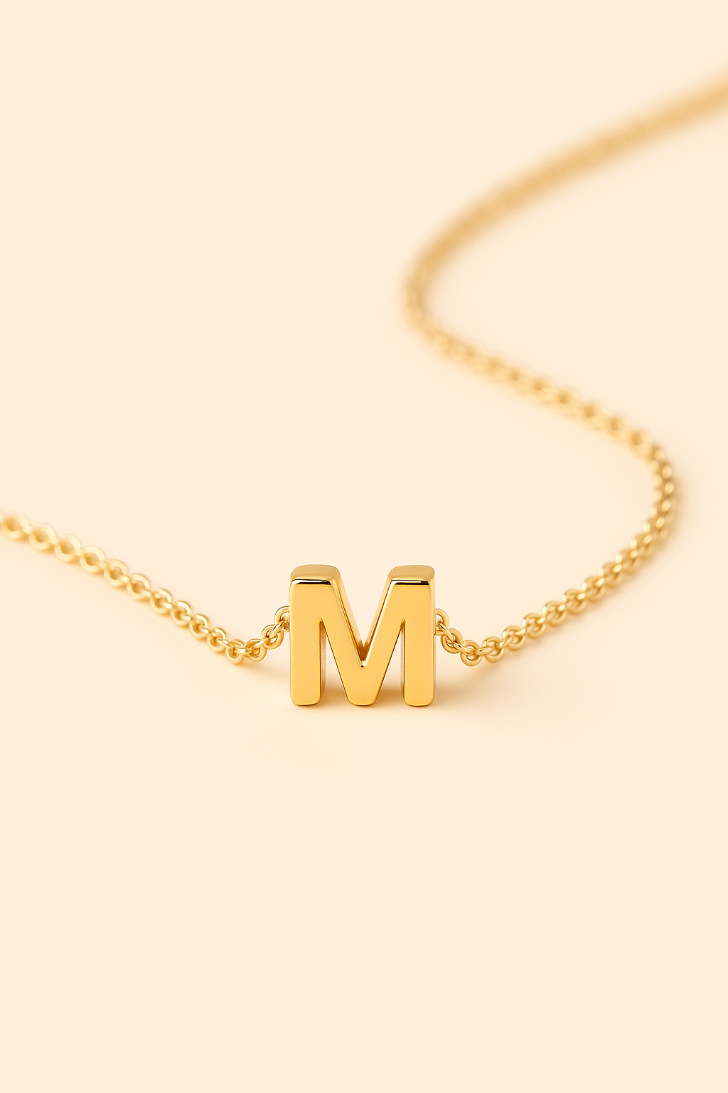 Gold necklace with a 'M' pendant on a beige background