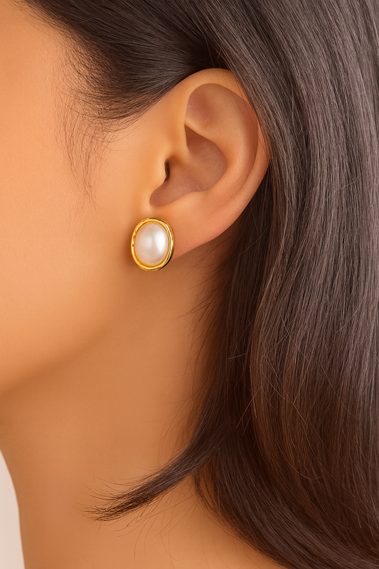 Close-up of an ear wearing a gold earring with a pearl center.