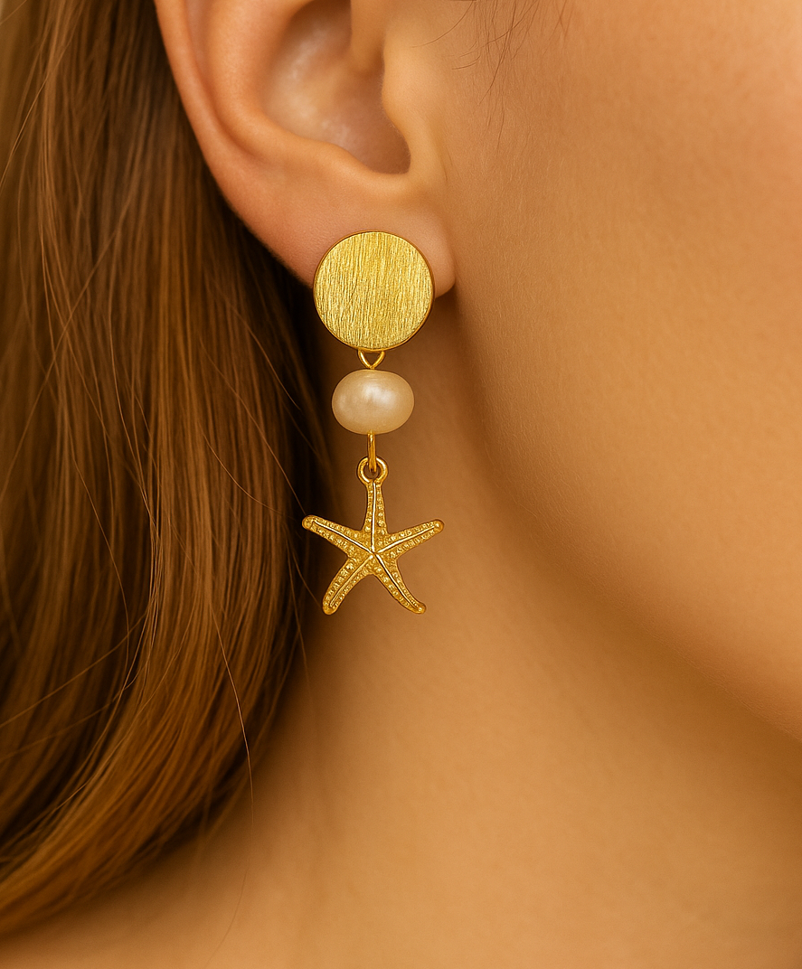 Gold earring with starfish and pearl detail worn by a person